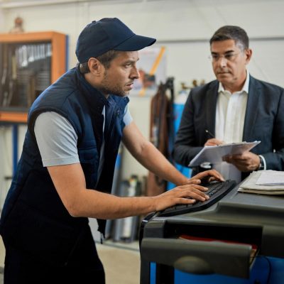 mid-adult-inspector-overseeing-auto-repairman-who-is-working-n-computer-workshop-focus-is-mechanic_637285-7568